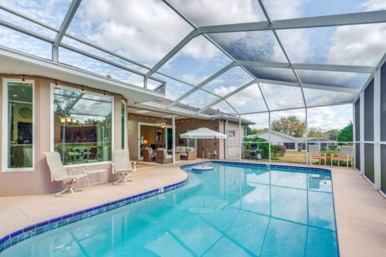 The pool deck at the Golf and Pool Home seen from the lanai end, with patio chairs under the screen and the house along the far side.