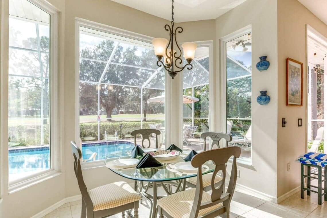 The breakfast nook at the Golf and Pool Home: a glass table laid for four in a bay of windows looking straight out at the screened pool.